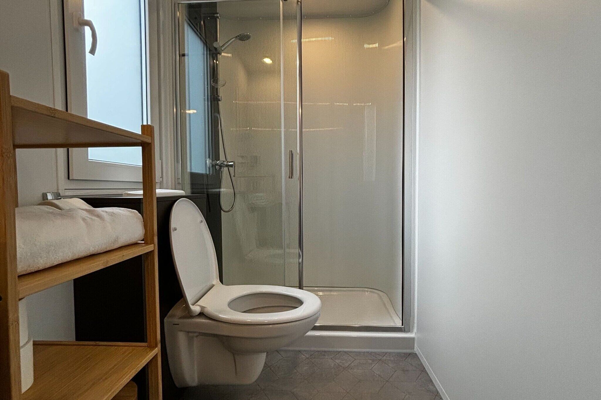 A modern bathroom with a shower, toilet, and a wooden shelf with towels.