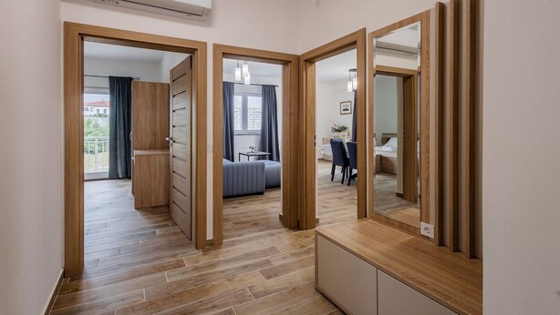 Moderni hotellihuone, jossa on puulattia, suuri peili, vaatekaappi ja sinisellä päätyosalla varustettu sänky.