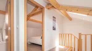 A spacious room with a wooden ceiling, a bed, and a staircase.
