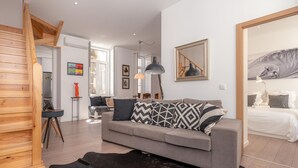 A modern living room with a grey sofa, a black rug, and wooden flooring.