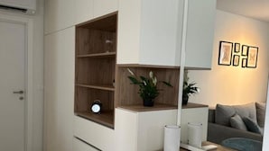 A modern living room with a built-in wooden shelf, a sofa, a coffee table, and a wall-mounted mirror. - One Bedroom Apartment with Balcony and City View (Zadar)