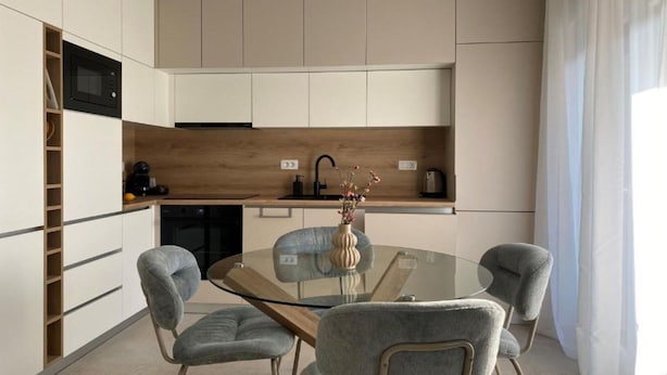 A modern kitchen with a glass dining table, grey upholstered chairs, and a wooden backsplash. - One Bedroom Apartment with Balcony and City View (Zadar)