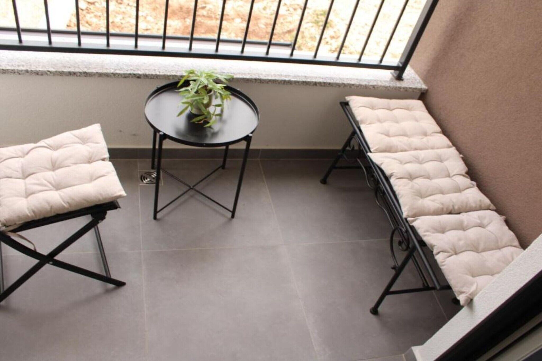 A balcony with two cushioned chairs and a small round table with a potted plant.