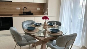 A modern kitchen with white cabinets, a wooden countertop, and a glass dining table with four grey chairs. - One Bedroom Apartment with Balcony and City View (Zadar)