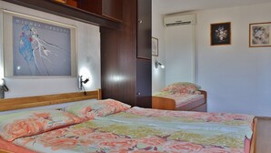 Een slaapkamer met een groot bed, een kleiner bed, een houten garderobe, een deur en een wandairconditioner.