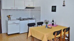 A compact kitchen with white cabinets, a stove, and a dining table with chairs. - Apartments Jug - Comfort Studio Apartment with Balcony and Sea View (Lopar)