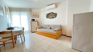 A compact living space with a dining table, a sofa, a refrigerator, and a microwave. - 5-Person Stay by the Beach (Porto Santa Margherita (VE))