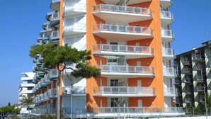 A multi-story residential building with balconies, a clear sky, and a tree in the foreground. - 5-Person Stay by the Beach (Porto Santa Margherita (VE))