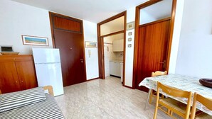 A compact room with a bed, a dining table with chairs, a kitchen area, and a wooden wardrobe. - 5-Person Stay by the Beach (Porto Santa Margherita (VE))