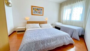 A hotel room with two beds, a wooden headboard, a small table, and a framed picture on the wall. - 5-Person Stay by the Beach (Porto Santa Margherita (VE))
