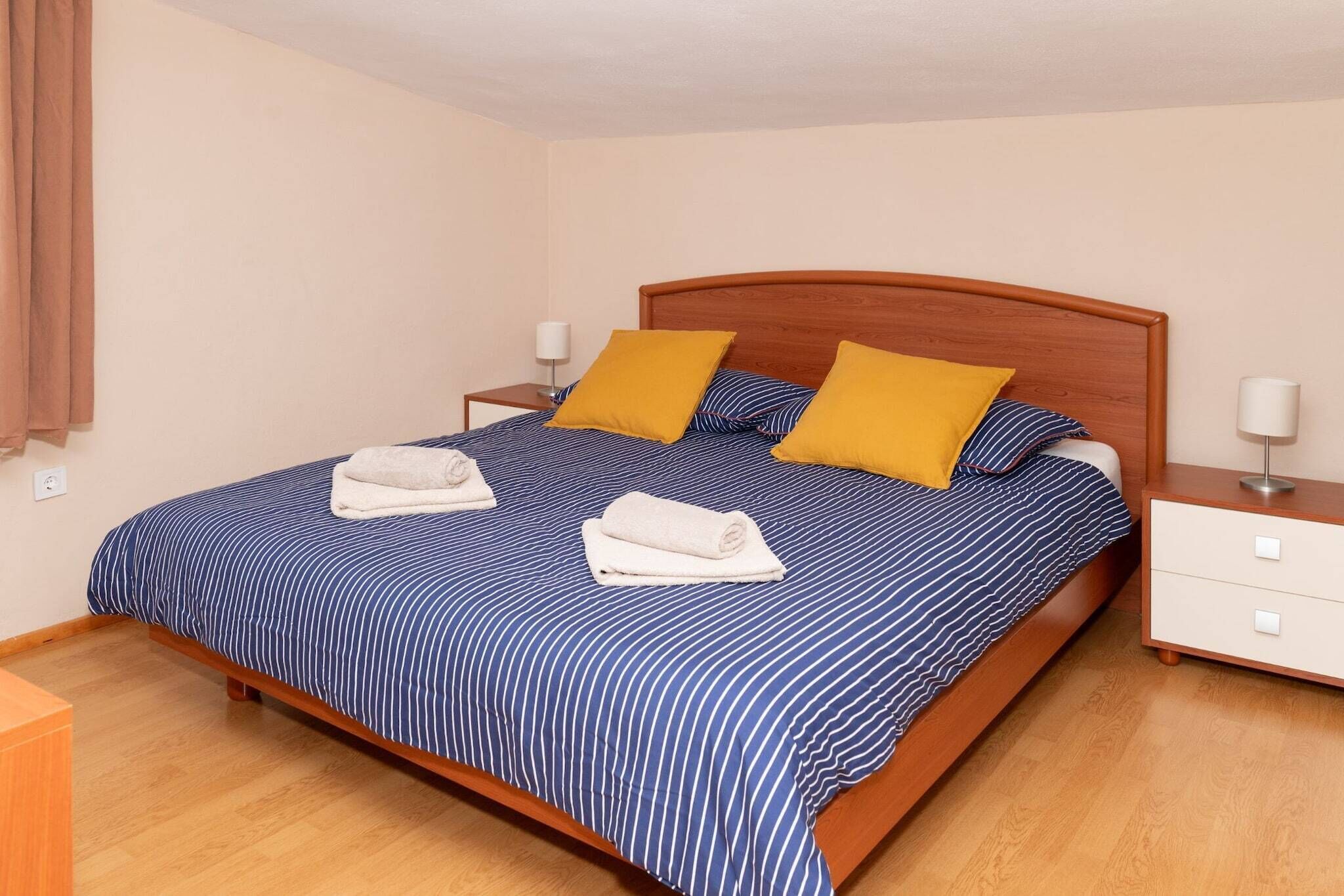 Een netjes opgemaakt bed met gestreept beddengoed, twee kussens en twee opgerolde handdoeken.