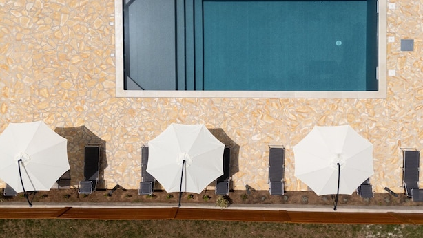 A swimming pool with a stone wall, three white umbrellas, and solar panels.