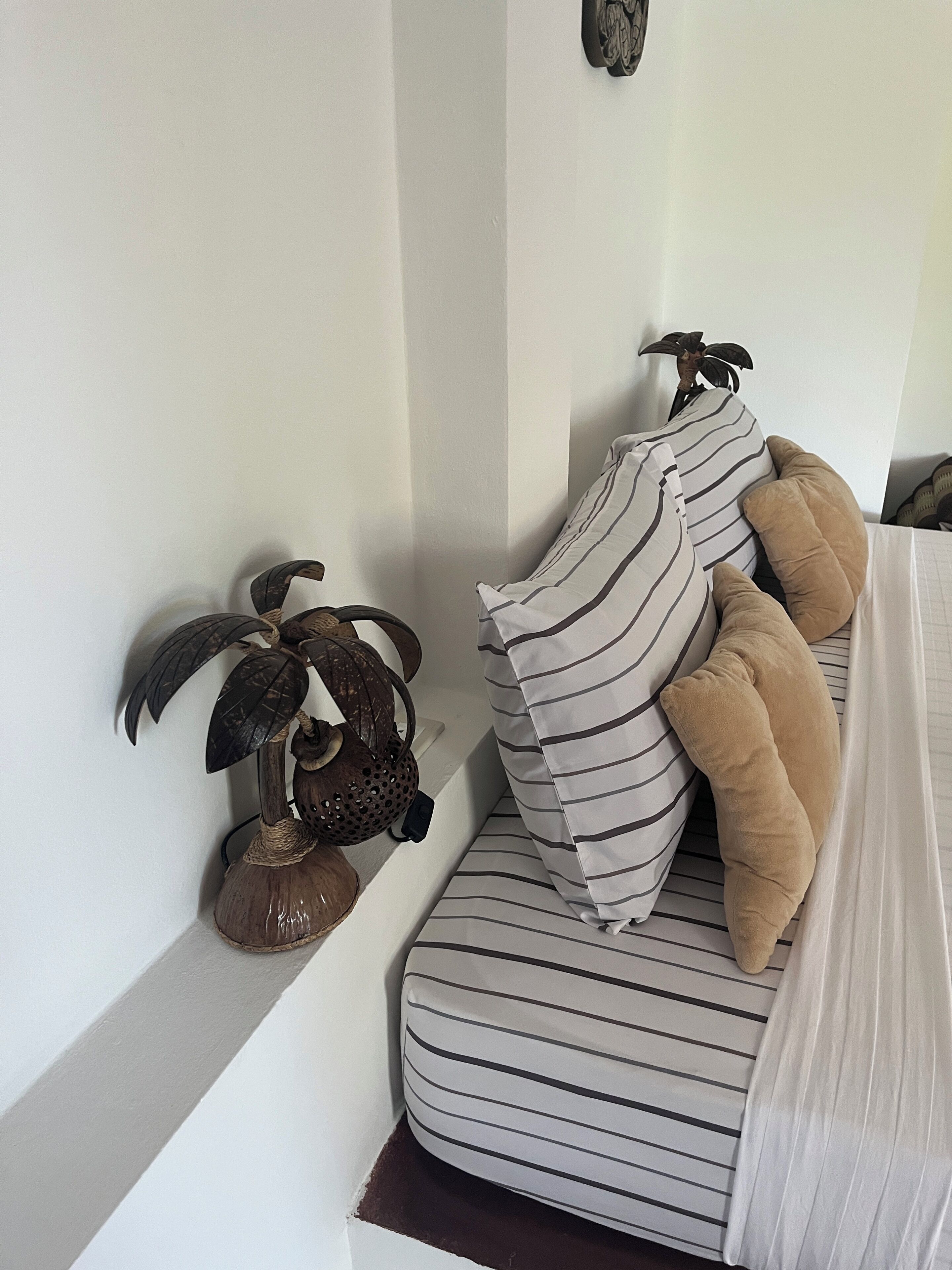 Un coin de pièce avec un canapé à rayures, une plante décorative et un luminaire fixé au mur.