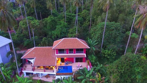 A two-story house with a red roof, surrounded by dense tropical vegetation. - PINK HOUSE (Koh Samui)