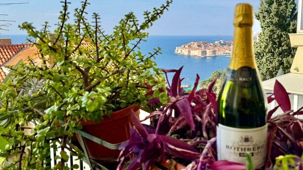 A balcony with a bottle of wine, potted plants, and a view of a coastal town. - Charming Apartment with Terrace and Old Town View - One Bedroom Apartment with Terrace (Dubrovnik)