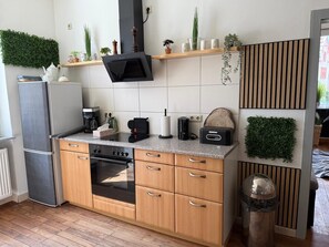 Una cocina moderna con armarios de madera, horno empotrado, cafetera y varias plantas en estantes.