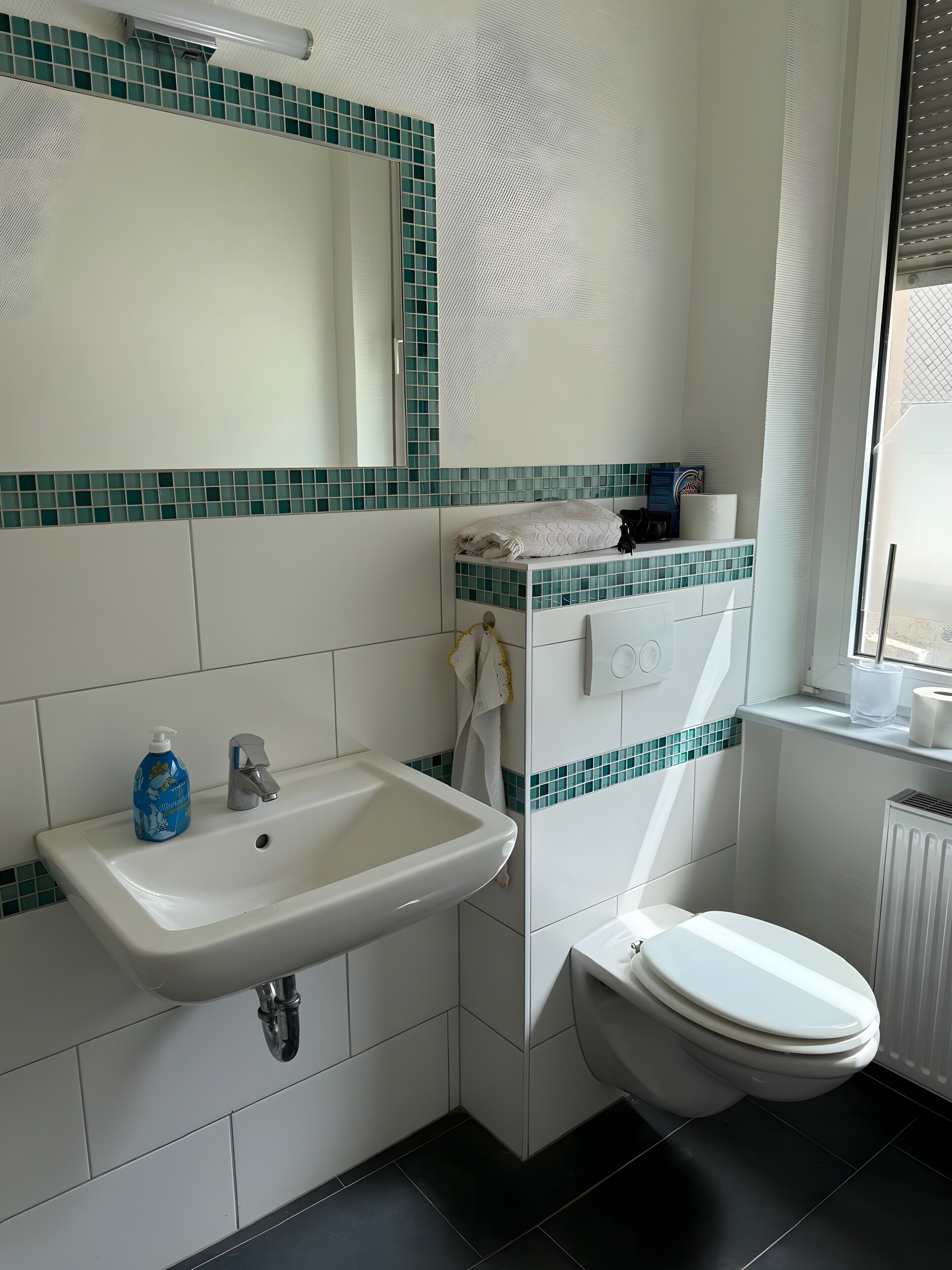 Een badkamer met een wit wastafelmeubel, een spiegel, een toilet en een raam.