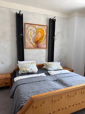 Un dormitorio con una cama, dos mesitas de noche, un cabecero de madera, un cuadro y una lámpara de pared.