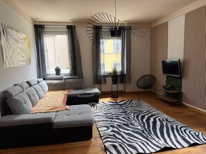 A modern living room with a sectional sofa, a zebra-patterned rug, a floor lamp, and a TV stand. - Apartment 'Neunkirchen City' with Wi-Fi (Neunkirchen)