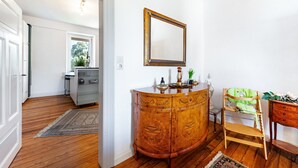 A room with a wooden floor, a white wall, a wooden cabinet with a mirror, a green chair, and a small table with decorative items.