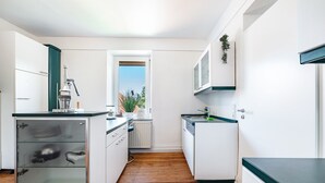A modern kitchen with white cabinets, a wooden floor, and a window providing natural light.