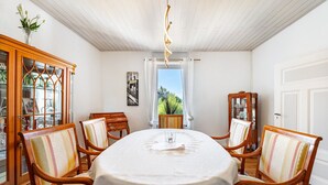 A dining area with a round table, four chairs, a cabinet with glass doors, and a view through a window.