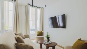 A modern living room with a beige sofa, a round coffee table, and a mounted flat-screen TV. - Elegant apartment - 3BR-8P- Le Marais (Paris)
