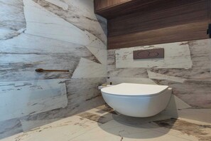 A bathroom with a toilet, marble walls, and a wooden panel.