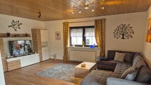 Una sala de estar moderna con una televisión de pantalla plana, un sofá gris, una mesa de centro y una ventana con cortinas.