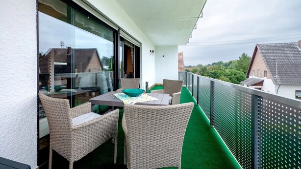 Un balcón con mobiliario de mimbre, una mesa y vistas a casas vecinas.
