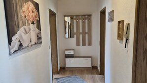 Un pasillo con suelo de madera, pared blanca, techo de madera, un espejo, una consola blanca y una puerta.
