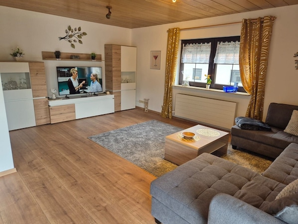 Un salon moderne avec un canapé, une table basse, un téléviseur et une fenêtre avec des rideaux.