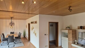 Una sala de estar moderna con techo de madera, un comedor con mesa y sillas, y un televisor sobre un mueble de madera.