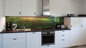 A modern kitchen with white cabinets, a stainless steel range, and a large backsplash. - Apartment 'Mit 65qm' with Private Terrace, Private Garden and Wi-Fi (Vogtsburg)