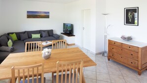 A modern living room with a sofa, a dining table, chairs, a TV, and a cabinet. - Apartment 'Mit 65qm' with Private Terrace, Private Garden and Wi-Fi (Vogtsburg)