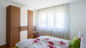 A bedroom with a bed, a wooden wardrobe, a chair, and a window with sheer curtains. - Apartment 'Mit 65qm' with Private Terrace, Private Garden and Wi-Fi (Vogtsburg)