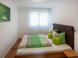 Une chambre à coucher comprenant un lit, une tête de lit, une table de chevet, une fenêtre avec des rideaux et un tableau accroché au mur.