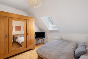 A bedroom with a large wardrobe, a television on a small table, and a skylight.