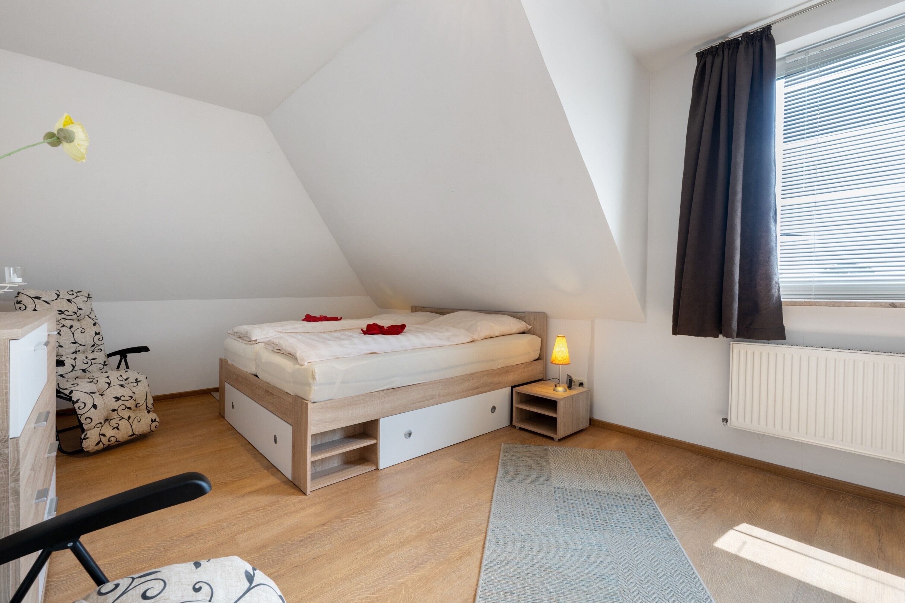 A bedroom with a loft bed, a desk, a chair, a radiator, and a window with curtains.