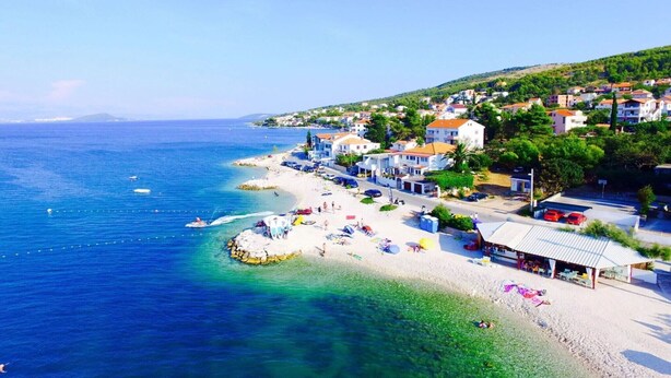 Une ville côtière avec une plage, des maisons et une mer d’un bleu limpide.