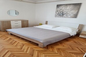A bedroom with a bed, a bedside table, a lamp, a dresser, and a wall-mounted mirror.