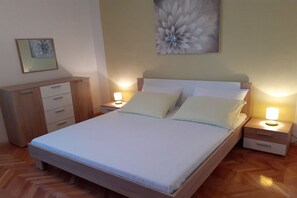 A neatly made bed with two pillows, a bedside table with a lamp, and a wooden dresser with drawers. - Apartment Ivica - Three Bedroom Apartment with Terrace (Arbanija)