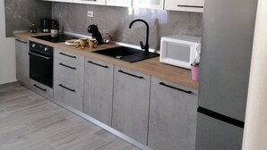 Une cuisine moderne avec des meubles gris, un plan de travail en bois, un évier noir, un micro-ondes blanc et un réfrigérateur en acier inoxydable.