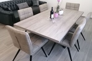 A dining area with a light wood table, grey upholstered chairs, a black bottle, and a pink flower pot. - Apartment Ivica - Three Bedroom Apartment with Terrace (Arbanija)