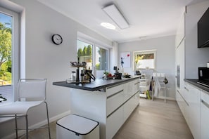 A modern kitchen with a central island, white cabinetry, and a window providing a view of greenery outside. - Holiday Home 'Alte Tischlerei' with Private Terrace, Shared Garden and Wi-Fi (Hemmingstedt)