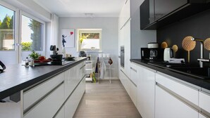 Ett modernt kök med vita skåp, en svart bänkskiva och ett fönster med utsikt över grönområden.