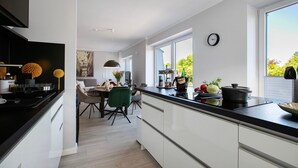 Ett modernt kök med en svart bänkskiva, vita skåp och en matplats med en grön stol.