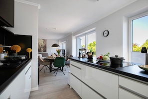 Une cuisine moderne avec un plan de travail noir, des placards blancs et un coin repas agrémenté d’une chaise verte.