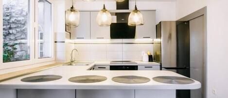 A modern kitchen with a central island, pendant lights, and a large window.