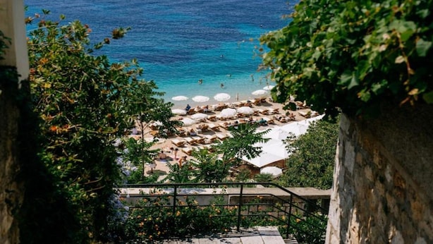 A coastal view with a beach, umbrellas, and a stone staircase leading down to the beach.